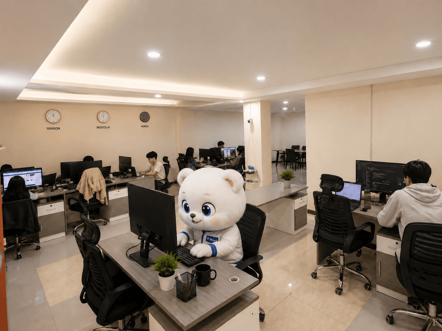 The ITWizard Myanmar office in Yangon — the team at work, the mascot at a desk in the foreground, and clocks showing Yangon, Mongolia and Korea time
